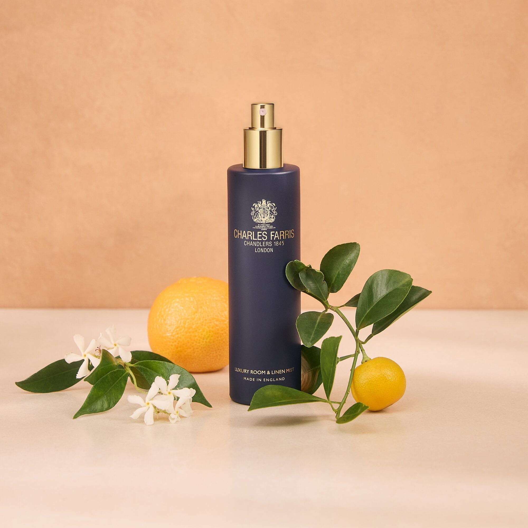 A bottle of Charles Farris Sweet Elixir orange blossom jasmine scented room spray fragrance home mist with mimosa, bergamot and honey styled with citrus fruits, green leaves, and white flowers.
