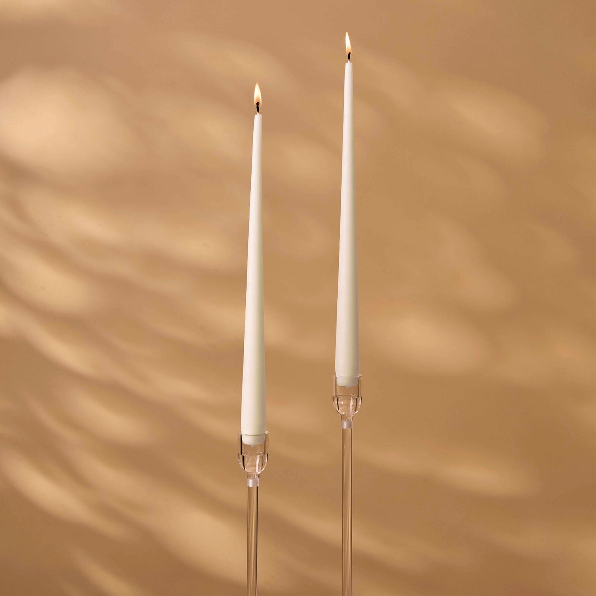 Charles Farris ivory tapered dinner candles, a lit pair in tall clear holders, made in England