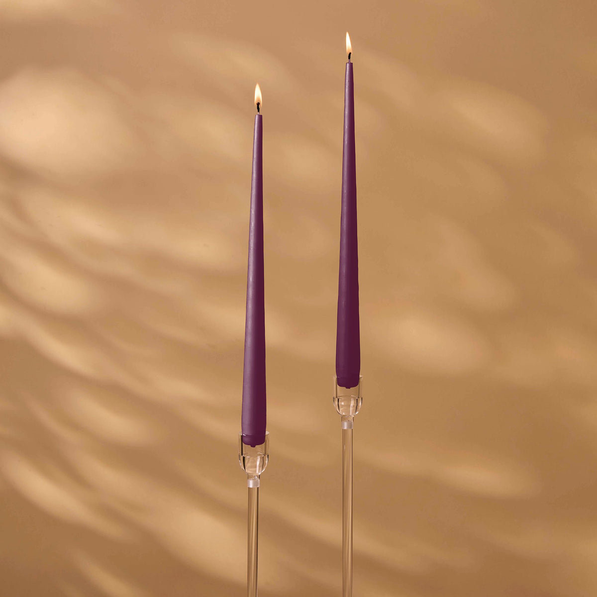 Charles Farris plum tapered dinner candles, a lit pair in tall clear holders, made in England