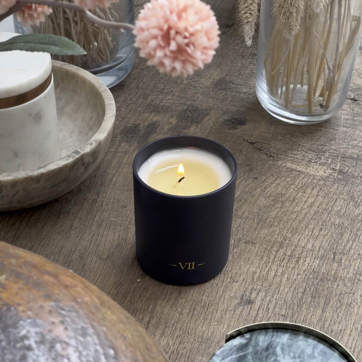 Candle in a black holder with 'VII' on a wooden surface with decorative elements.
