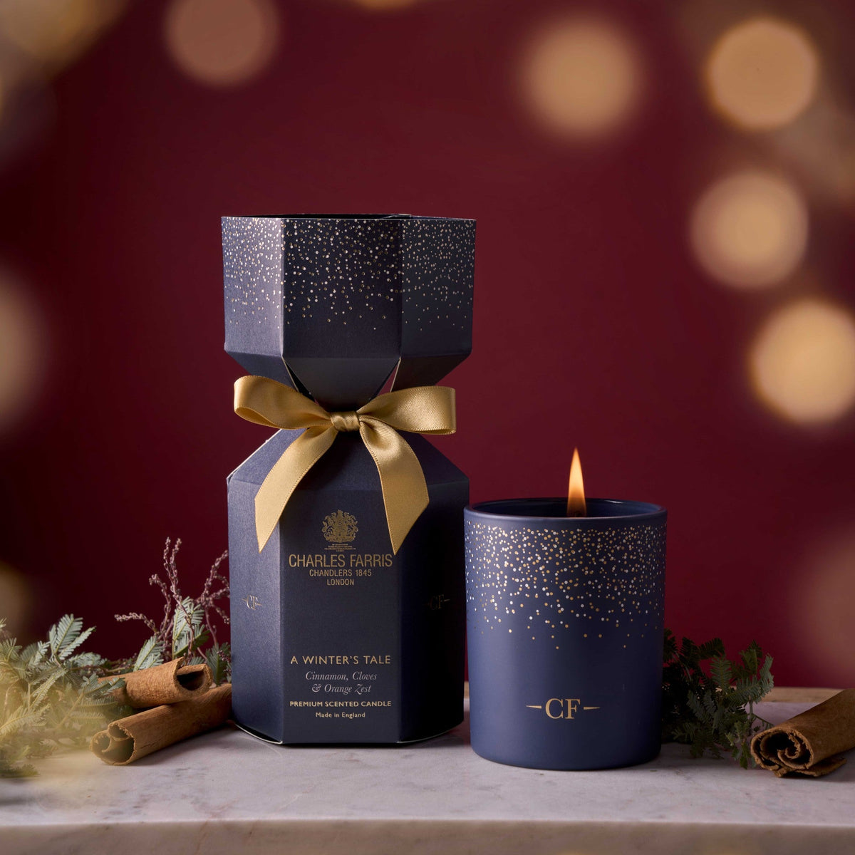 Charles Farris A Winter's Tale Christmas cracker candle beside a lit scented candle in a festive red setting