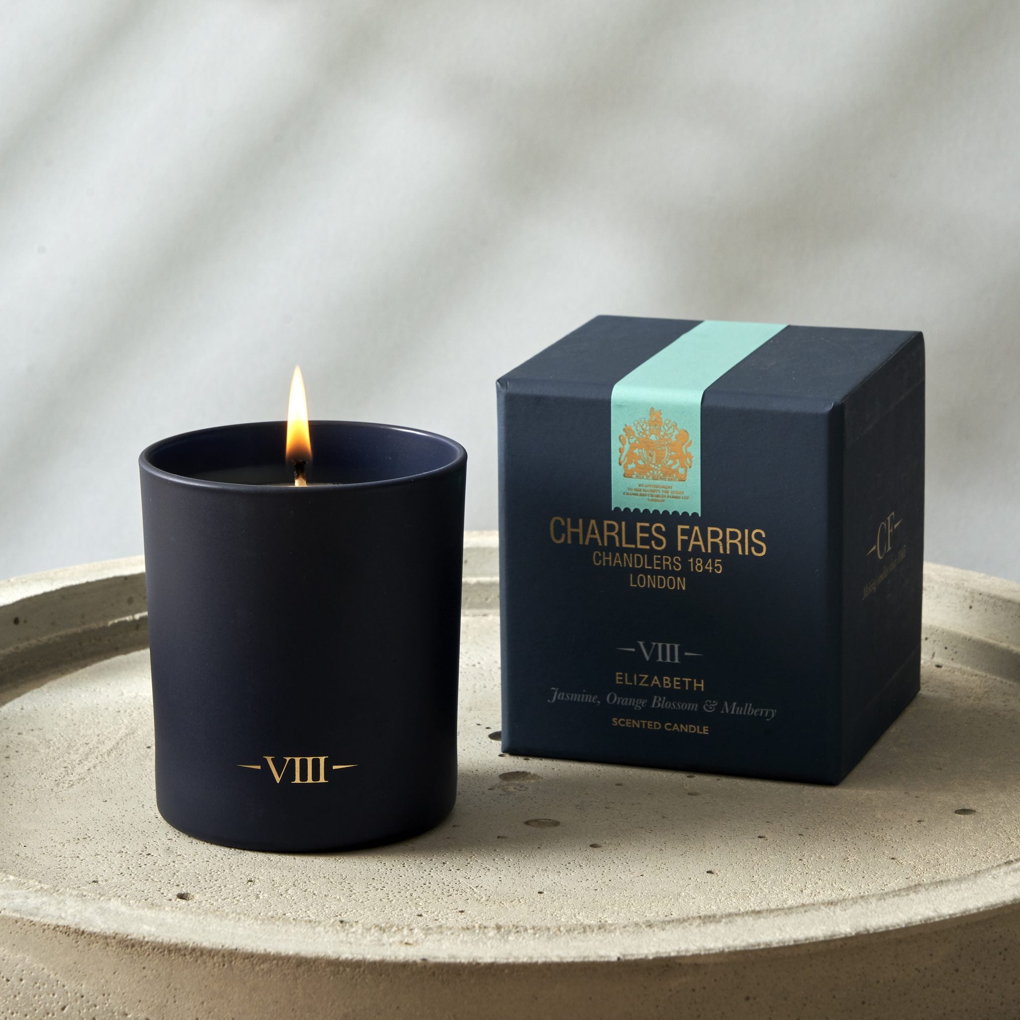 Black candle with a lit wick next to its packaging box on a neutral background