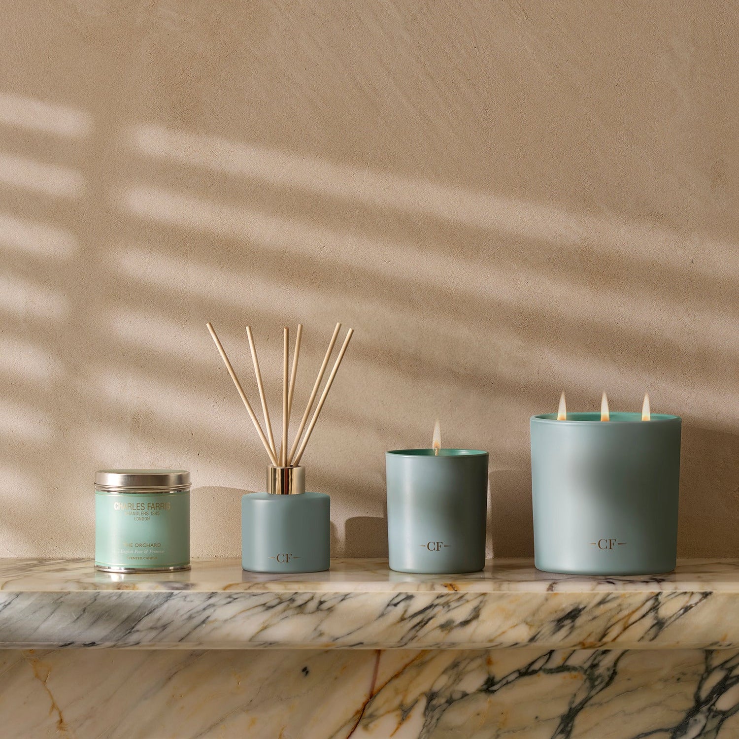 Set of candles and diffuser on a marble surface with a neutral wall background