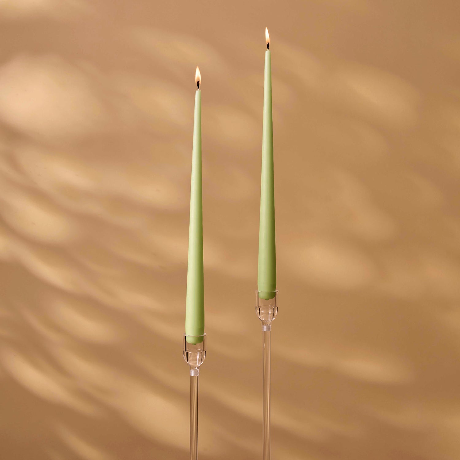 Two green candles in clear candle holders on a wooden surface with a beige wall background