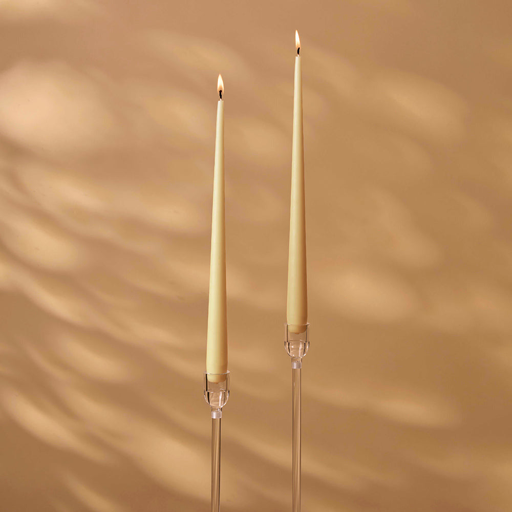 Two tall, thin candles with clear holders on a beige background