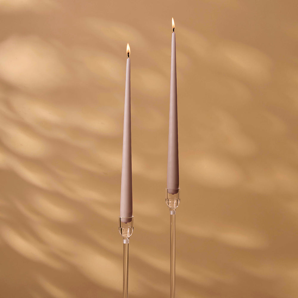 Two tall, thin candles with clear holders on a beige background