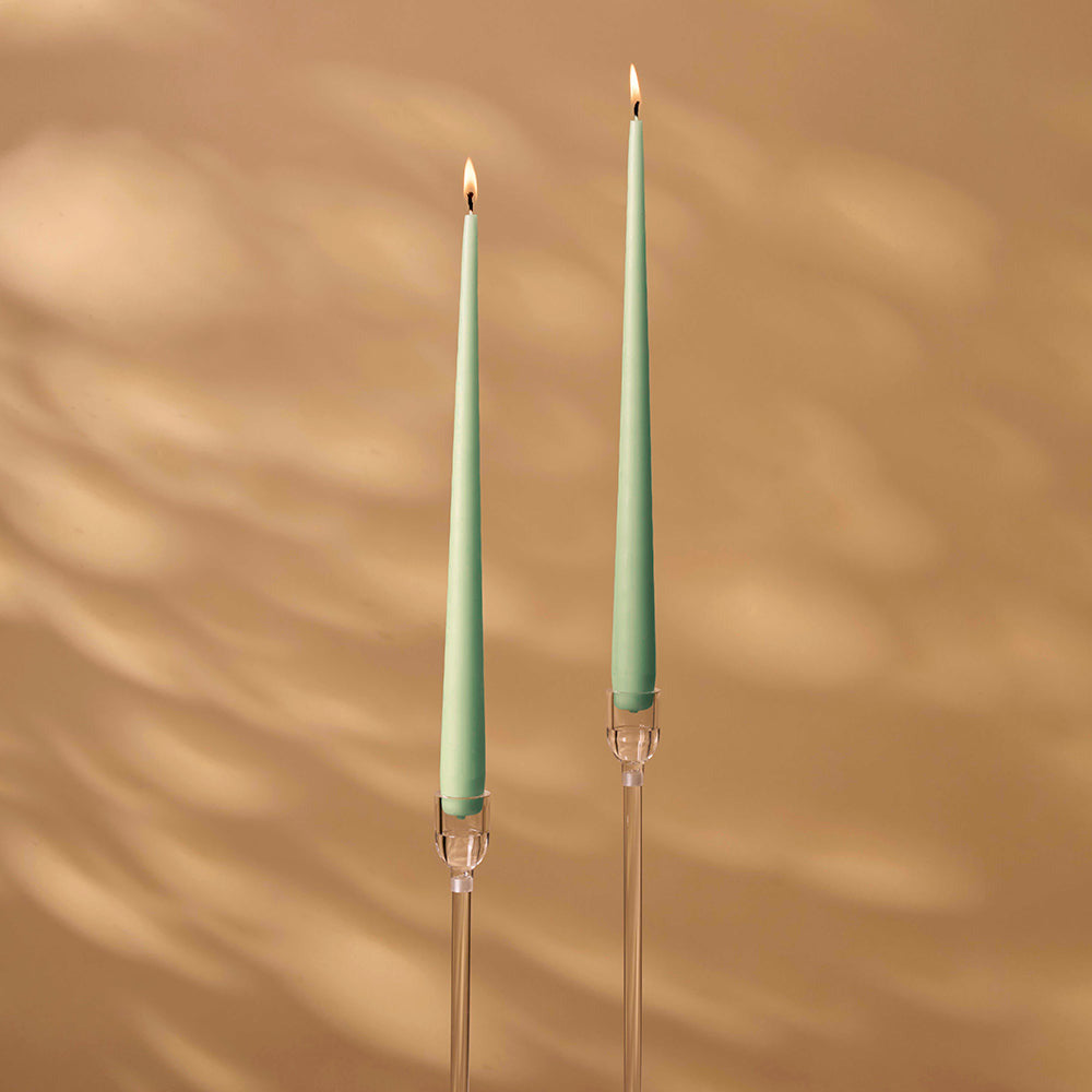 Two green candles with clear holders on a beige background