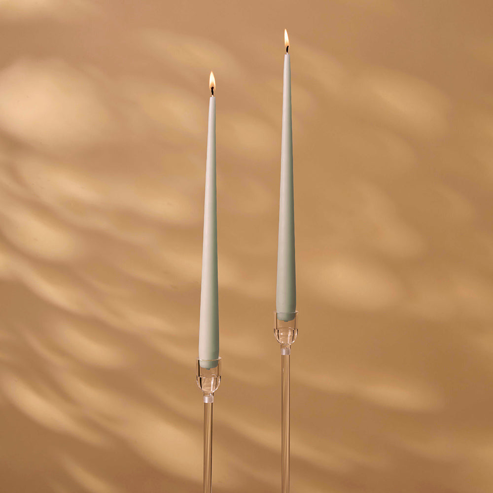 Two tall candle holders with lit candles on a beige wall background