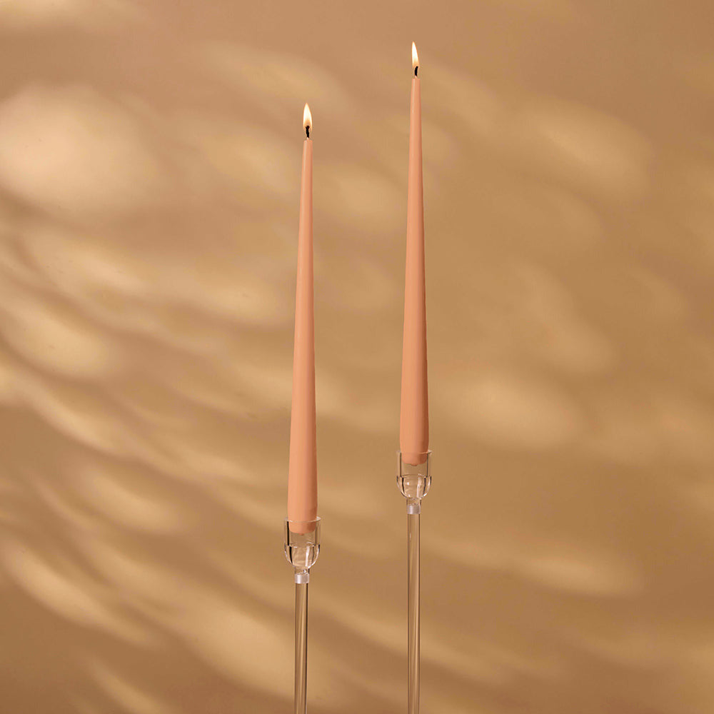 Two peach-colored candles with clear holders on a beige background