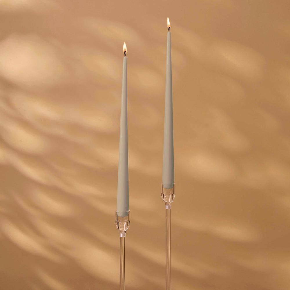Two tall, thin candles with decorative holders on a warm brown background