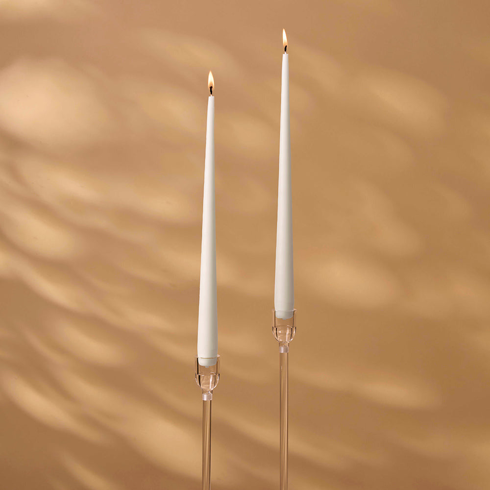 Two white candles with candle holders on a brown background