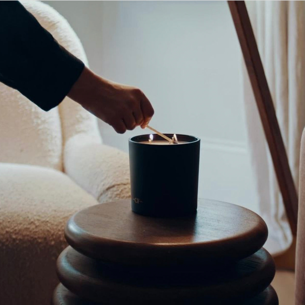 Person lighting a black candle on a wooden table with a soft, warm background