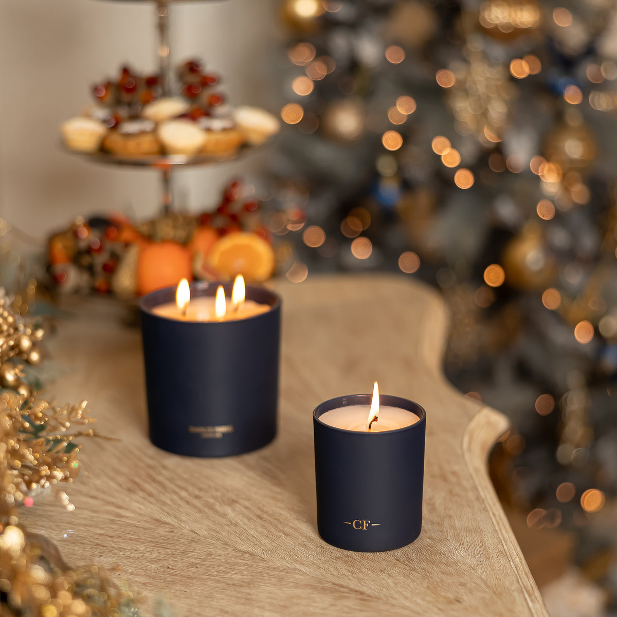 Two lit candles in navy holders on a wooden surface with a festive background.