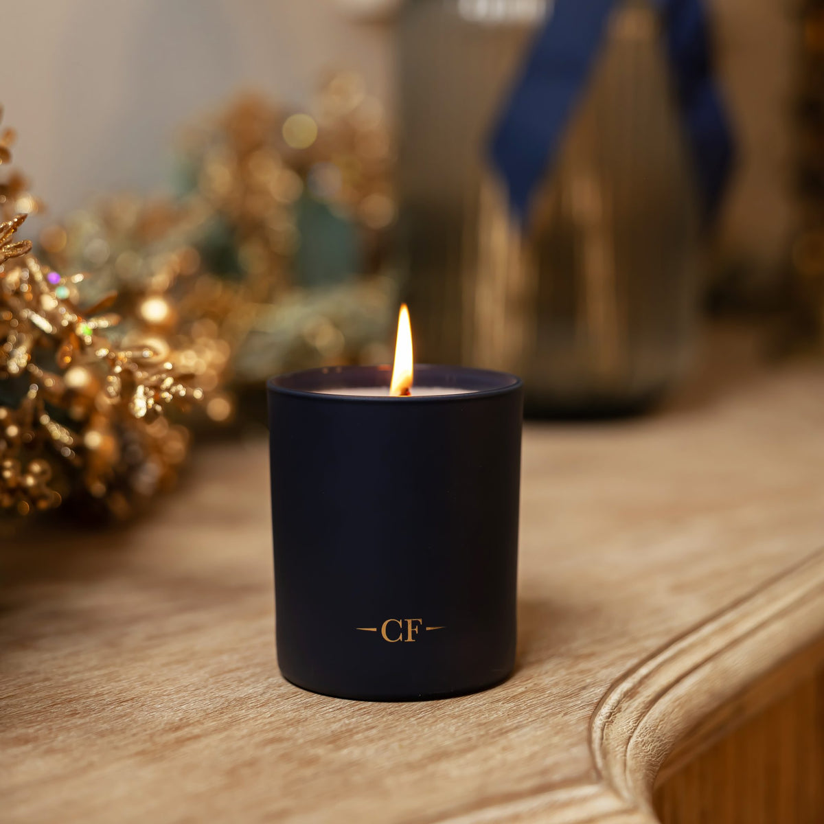 Blue candle with 'CF' initials on a wooden surface, blurred decorative background