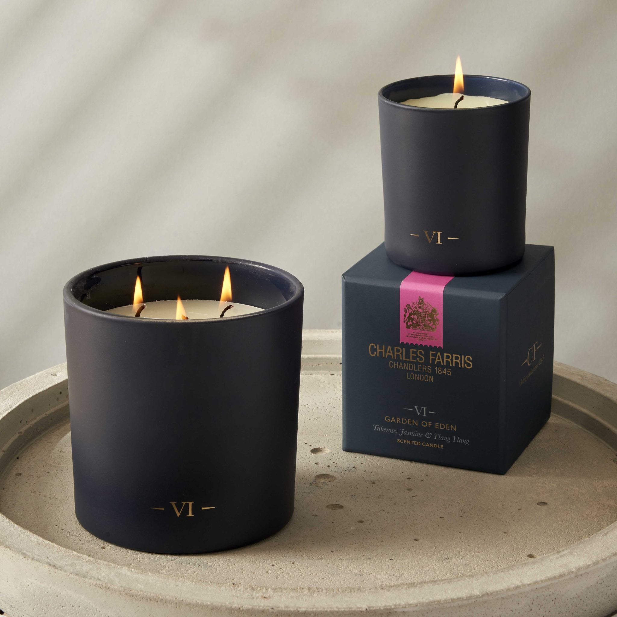 Two candles with visible flames and a box labeled 'Charles Farris' on a neutral background.