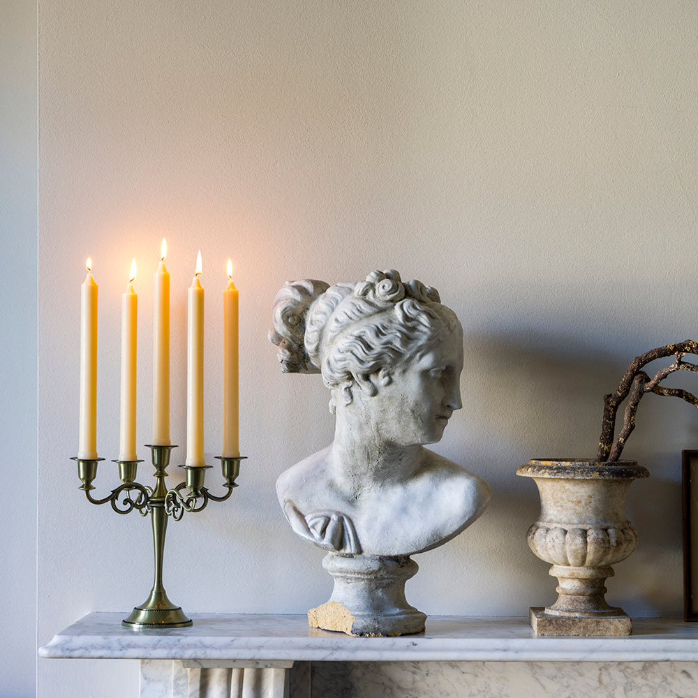 Bust of a classical figure, candle holder with lit candles, and decorative urn on a marble surface.