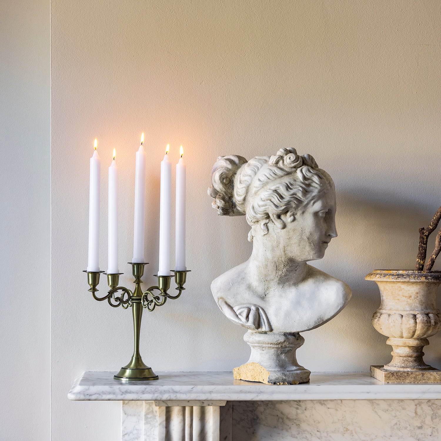 Bust of a classical figure, candle holder with lit candles, and decorative urn on a marble surface.