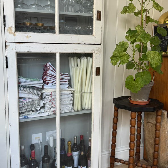 White cabinet with glass doors displaying folded clothes and bottles, as well as Charles Farris dining candles in glass containers.