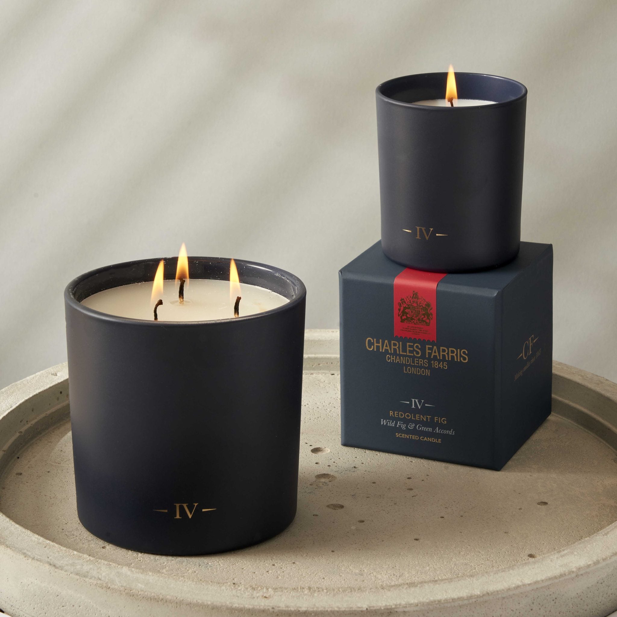 Two lit candles in black containers with a box labeled 'Charles Farris' on a stone surface.