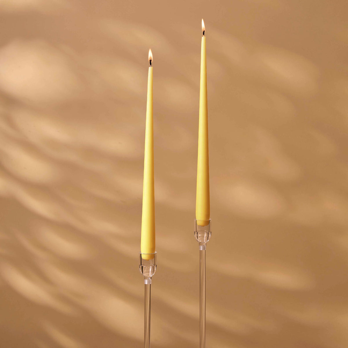 Charles Farris buttercup yellow tapered dinner candles, a lit pair in tall clear holders, made in England