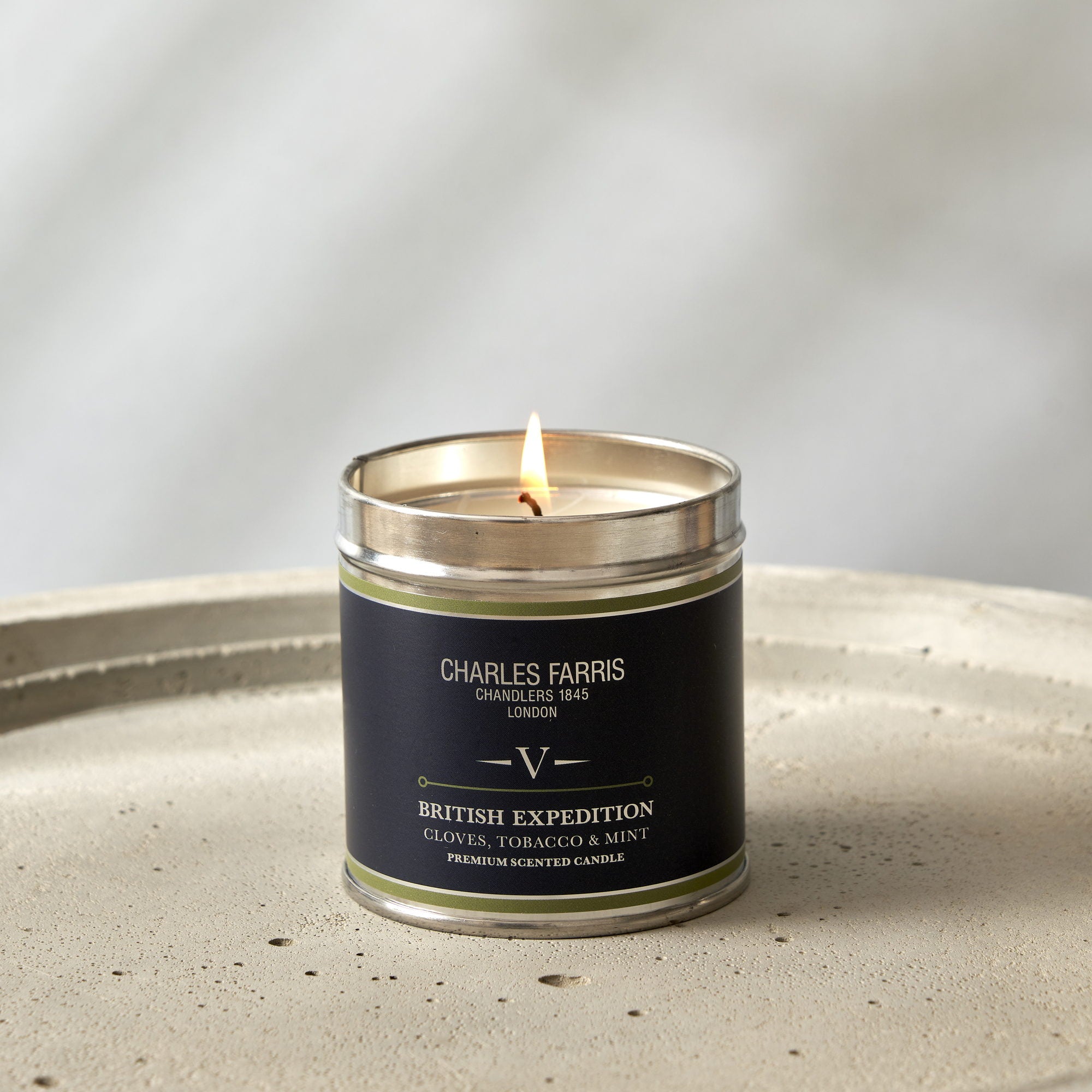 Charles Farris Grand Cascade signature tin candle burning on a concrete tray, scented with smoky cedar, moss and amber