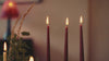 Hands lay an autumn dining table with striped linen, rust and olive napkins and amber glassware, then light and snuff red Charles Farris tapered dinner candles.