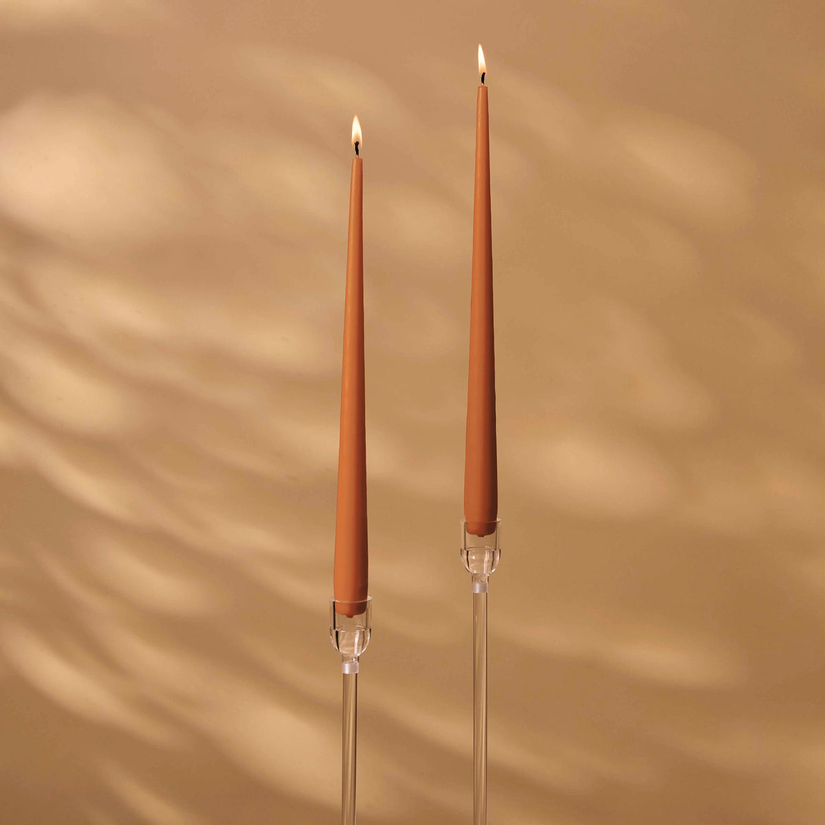Charles Farris terracotta tapered dinner candles, a lit pair in tall clear holders, made in England