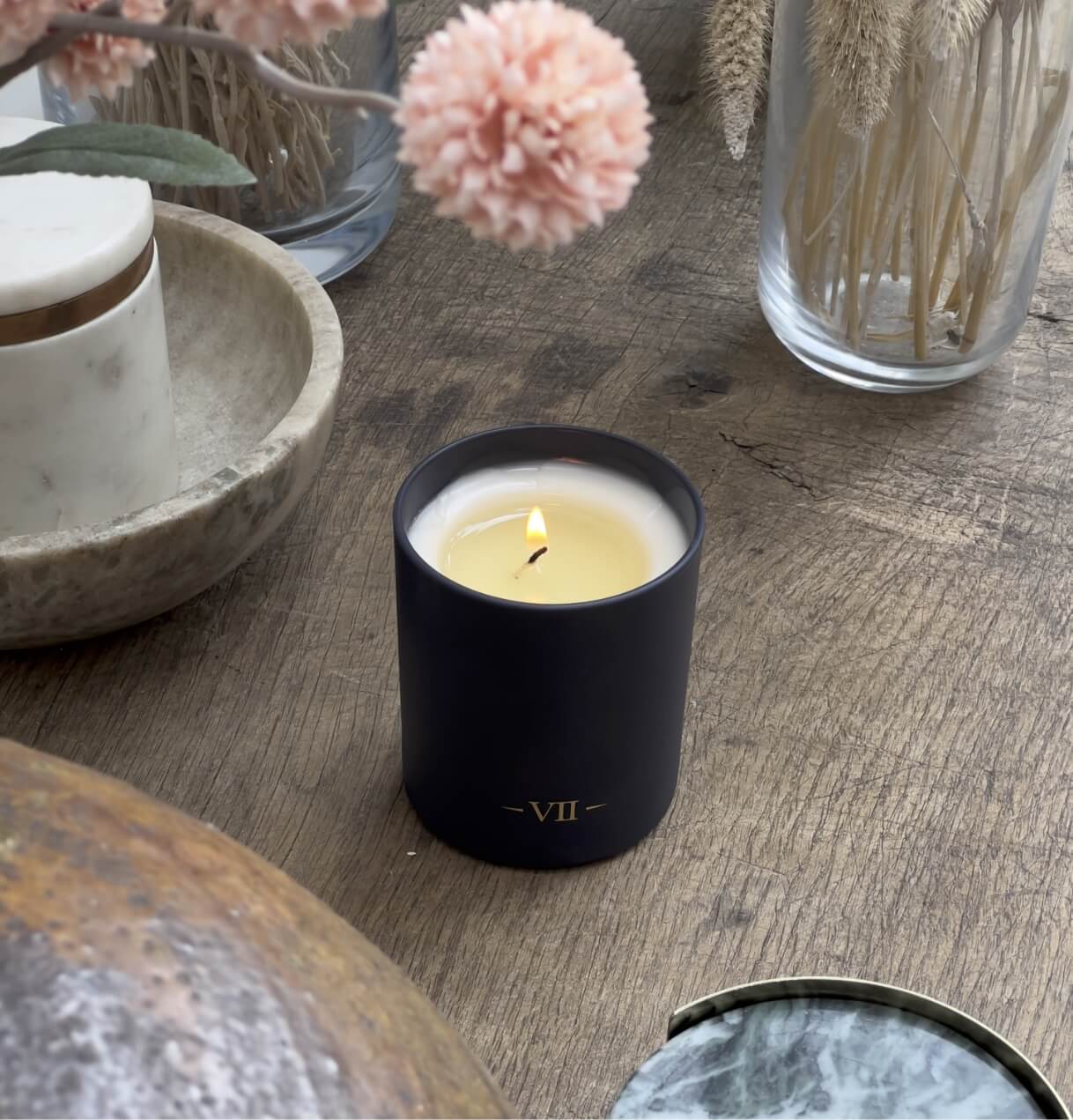 Candle in a black holder with 'VII' on a wooden surface with decorative elements.