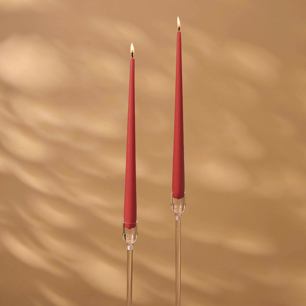 Charles Farris winter red tapered dinner candles, a lit pair in tall clear holders, made in England