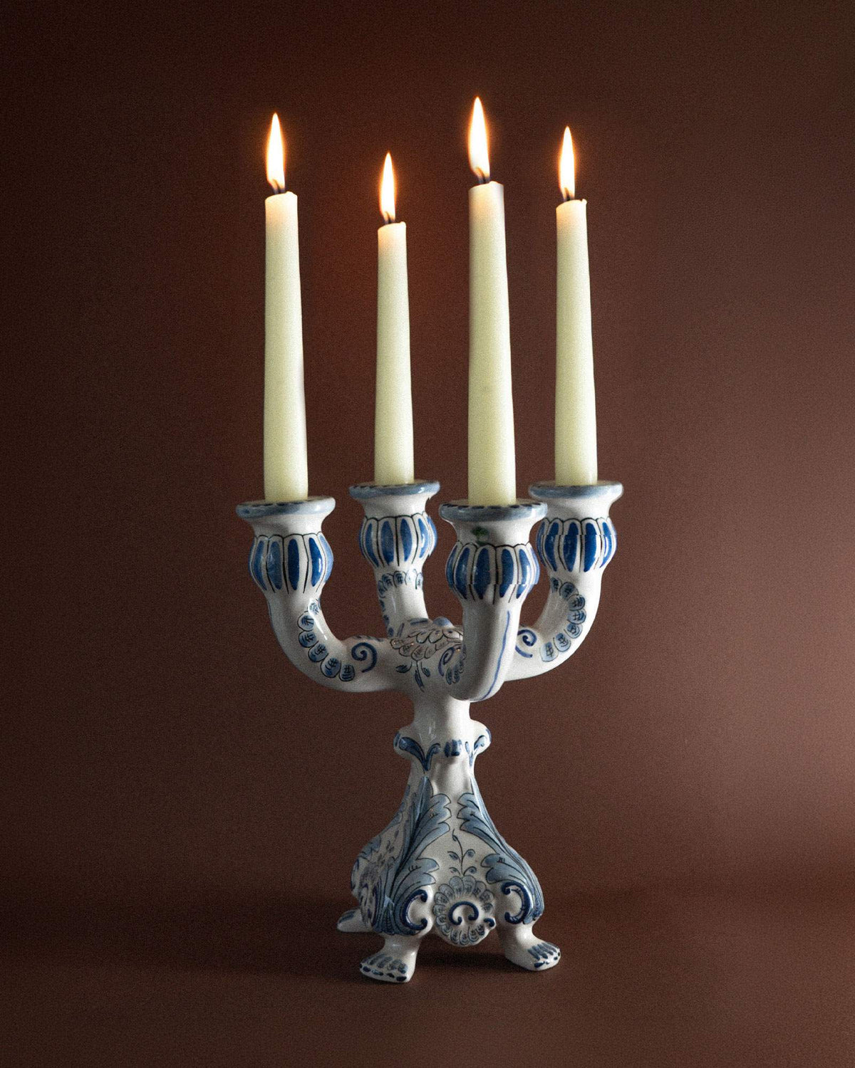 Four lit ivory dinner candles in a blue and white ceramic candelabra against a deep brown background